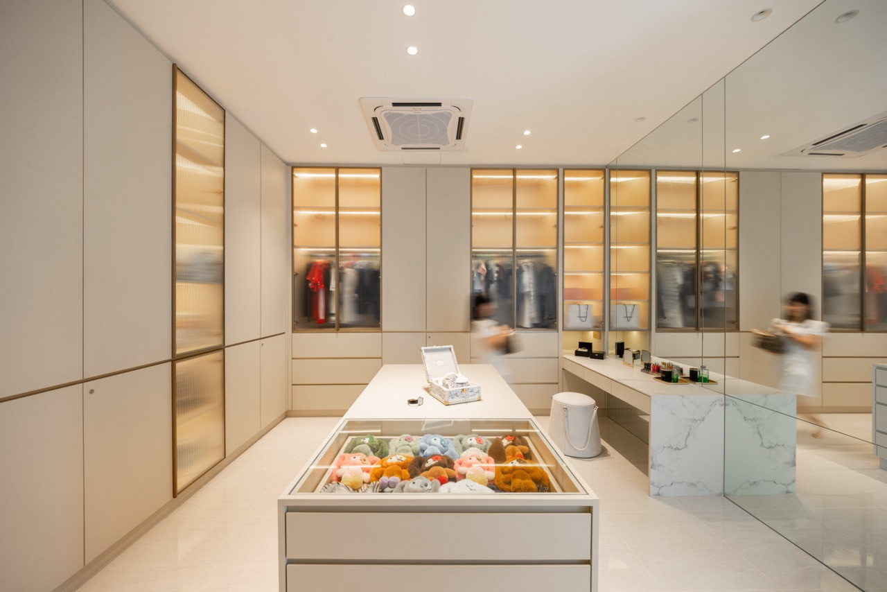 The walk-in wardrobe, with full-height cream cabinetry, bronze-framed glazed panels, a central island with a glass display top, and a marble vanity counter with floor-to-ceiling mirror