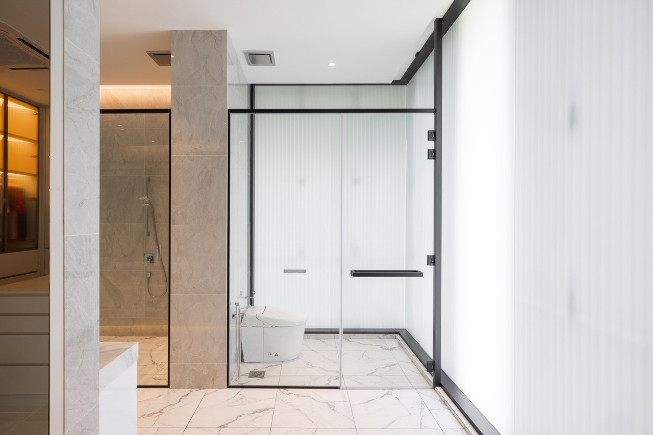 The master bathroom, with marble tiling, a walk-in shower, and black-framed fluted glass enclosure around the toilet area