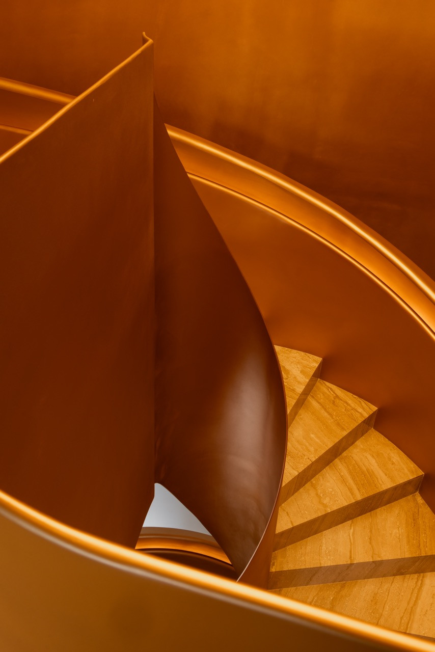 Detail of the bronze stringer and stone treads inside the spiral staircase, with the handrail profile visible above