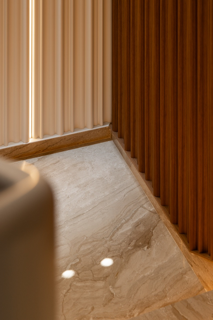 Detail of the stone treads, recessed step lighting, and the junction between the cream fluted panels and timber slat wall