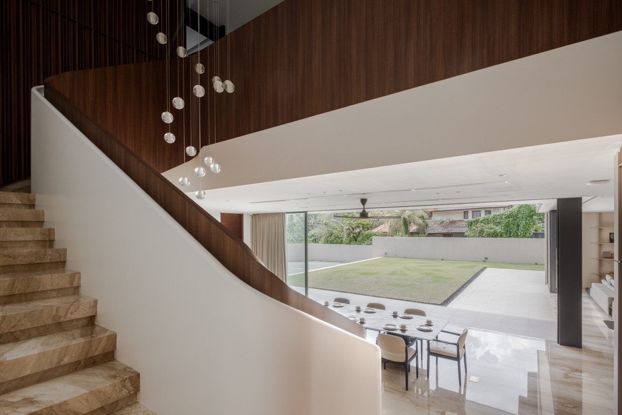 View from the staircase landing looking down to the dining area and lawn beyond, with the glass sphere pendant cluster above and the timber-clad staircase soffit