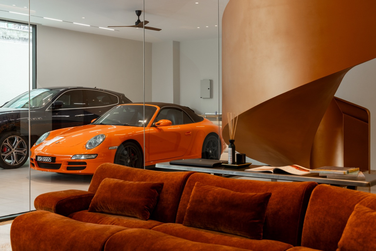 The car lounge interior, with an orange Porsche 911 visible through the glass partition and the base of the spiral staircase