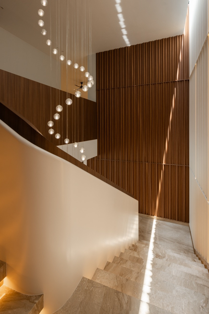 The main staircase corridor, with the glass sphere pendant cluster descending alongside the timber slat wall and backlit cream fluted panels lining the opposite side