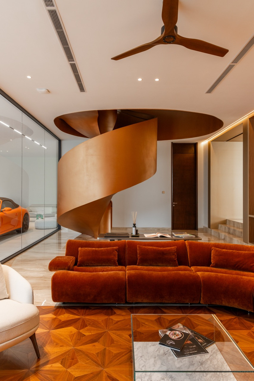 The car lounge, with the bronze spiral staircase rising to a circular ceiling recess, a rust-orange velvet sofa, and parquet flooring