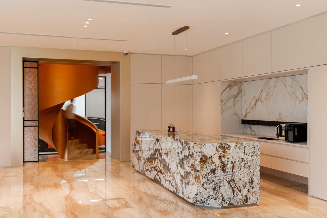 The kitchen with the heavily figured stone island, marble splashback, and cream cabinetry, with the spiral staircase visible through the doorway beyond