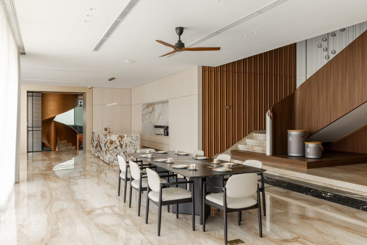 The dining area, with a dark stone table and white upholstered chairs; the kitchen island, timber staircase, and a glimpse of the spiral staircase are visible beyond