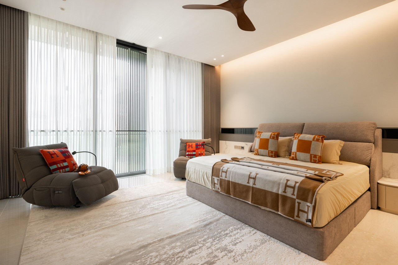 The master bedroom, with an upholstered bed, a lounge chair, and sheer curtains opening to the balcony