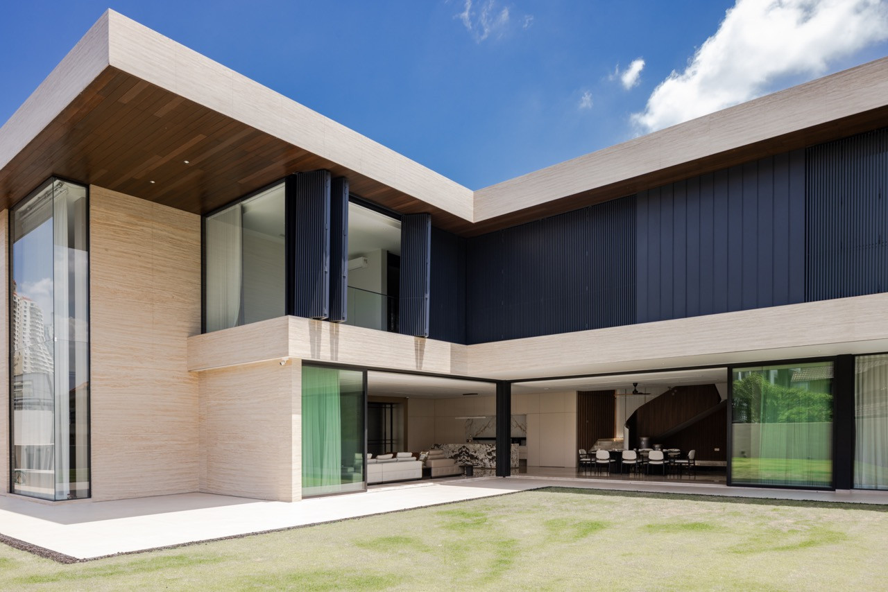 The corner of the L-shaped plan from the lawn, showing the living room and dining area both open to the terrace, with the spiral staircase visible through the glazing