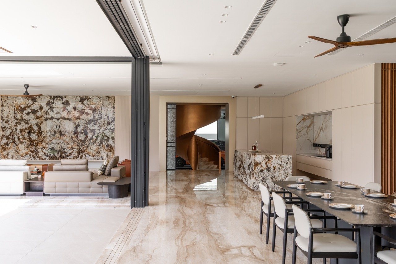 The ground floor open-plan interior, showing the dining table, kitchen island, feature marble wall, and a view through to the spiral staircase and car lounge beyond