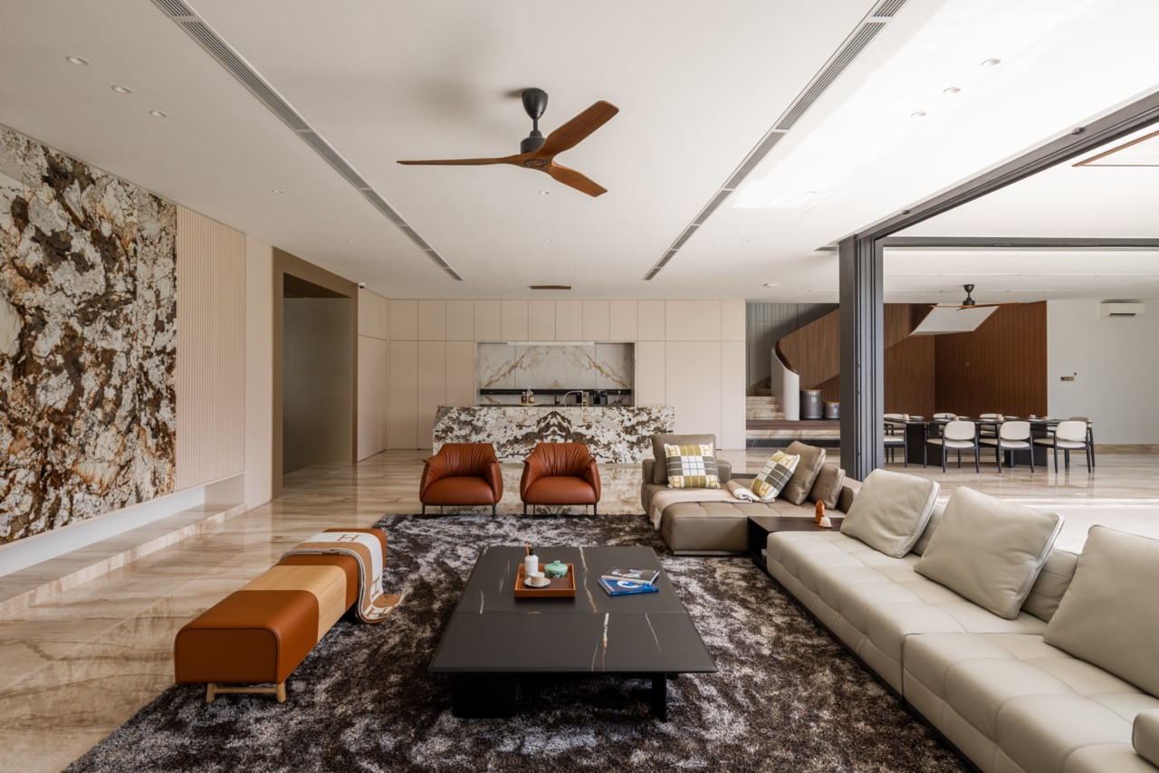 The living room showing the full-height figured stone feature wall, kitchen island, and a view through to the dining area and car lounge beyond