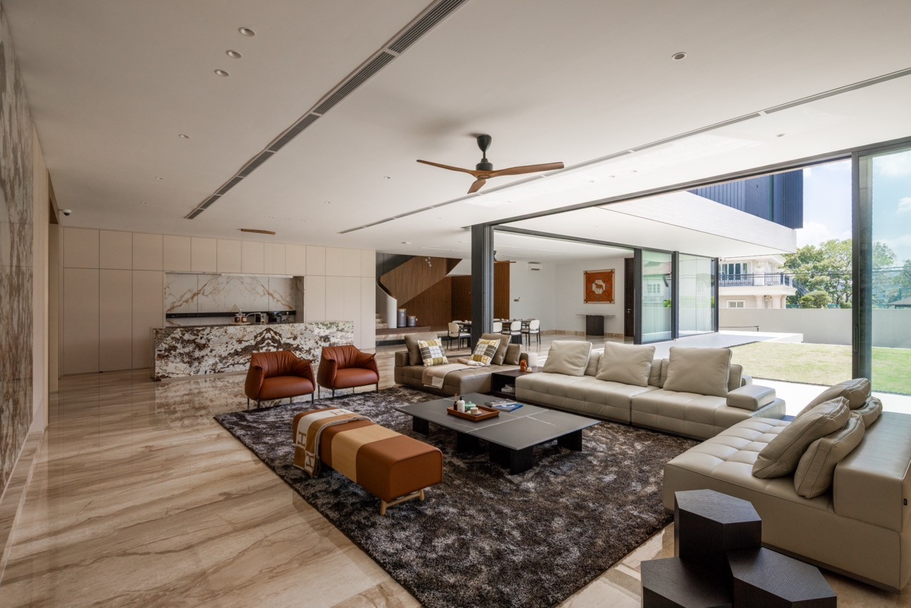 The living room, with the stone kitchen island in the background, leather armchairs, and full-height glazing opening to the courtyard and garden beyond
