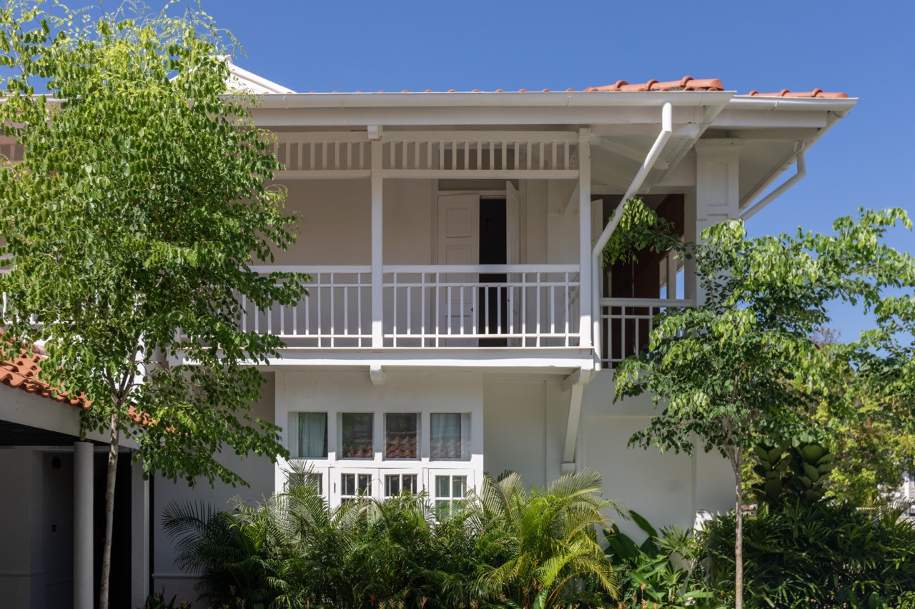 One of the complex’s secondary blocks, showing the simple white balustrade and deep verandah of the upper floor, with tropical planting at ground level