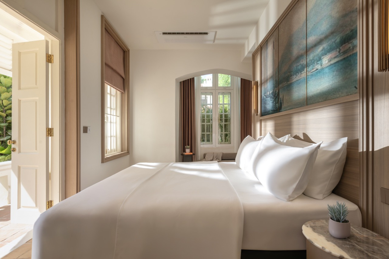 A Heritage Garden Patio Room bedroom, with the Penang harbour painting above the bed and the door open to the private patio beyond