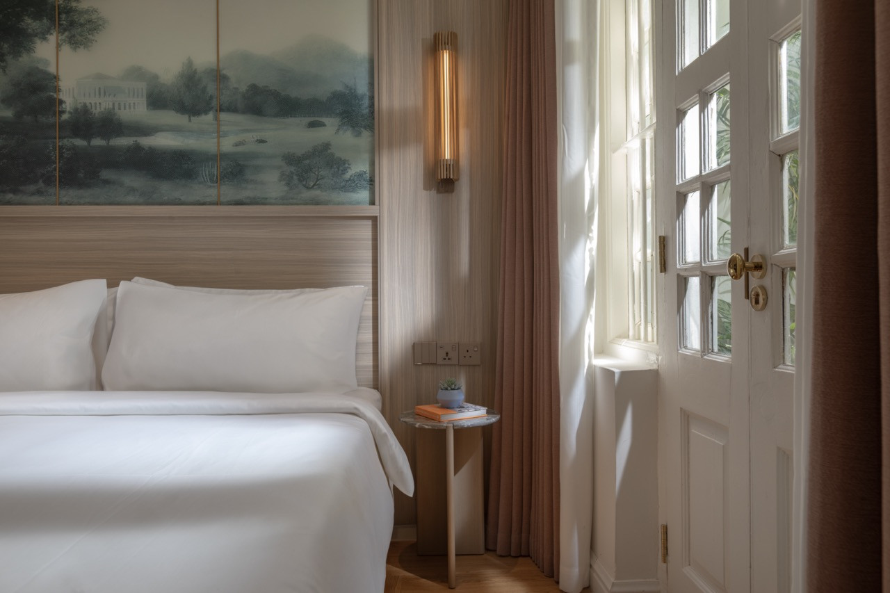A Heritage Room bedroom, with a landscape painting set into the timber headboard and the original glazed-panel door admitting afternoon light