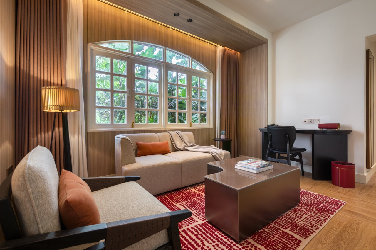 The Straits Suite living area, with a red-patterned rug, low coffee table and sofa grouped around the original arched window