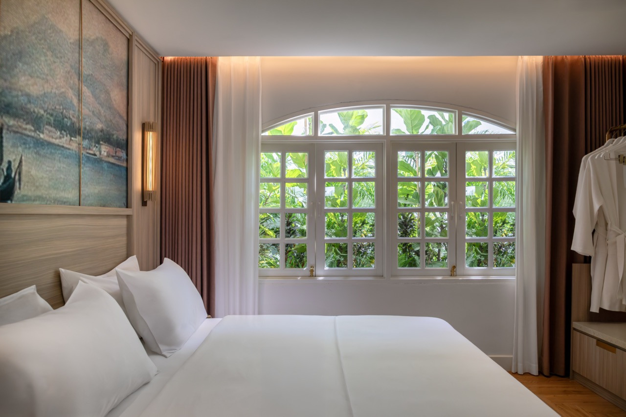 The Straits Suite master bedroom, with the arched original window framing a wall of tropical greenery beyond