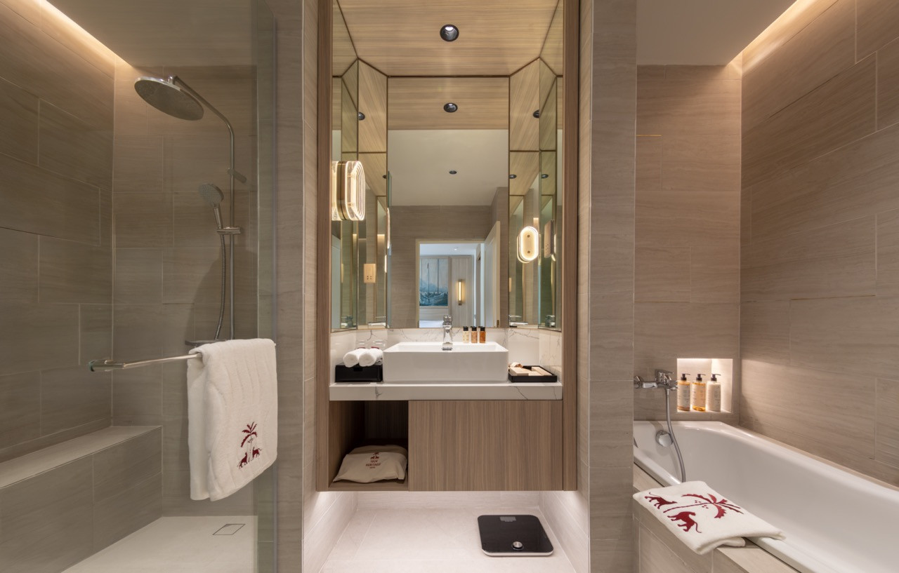 The Straits Suite bathroom, with rainfall shower, soaking tub and mirrored vanity; hotel towels embroidered with the palm and panther motif