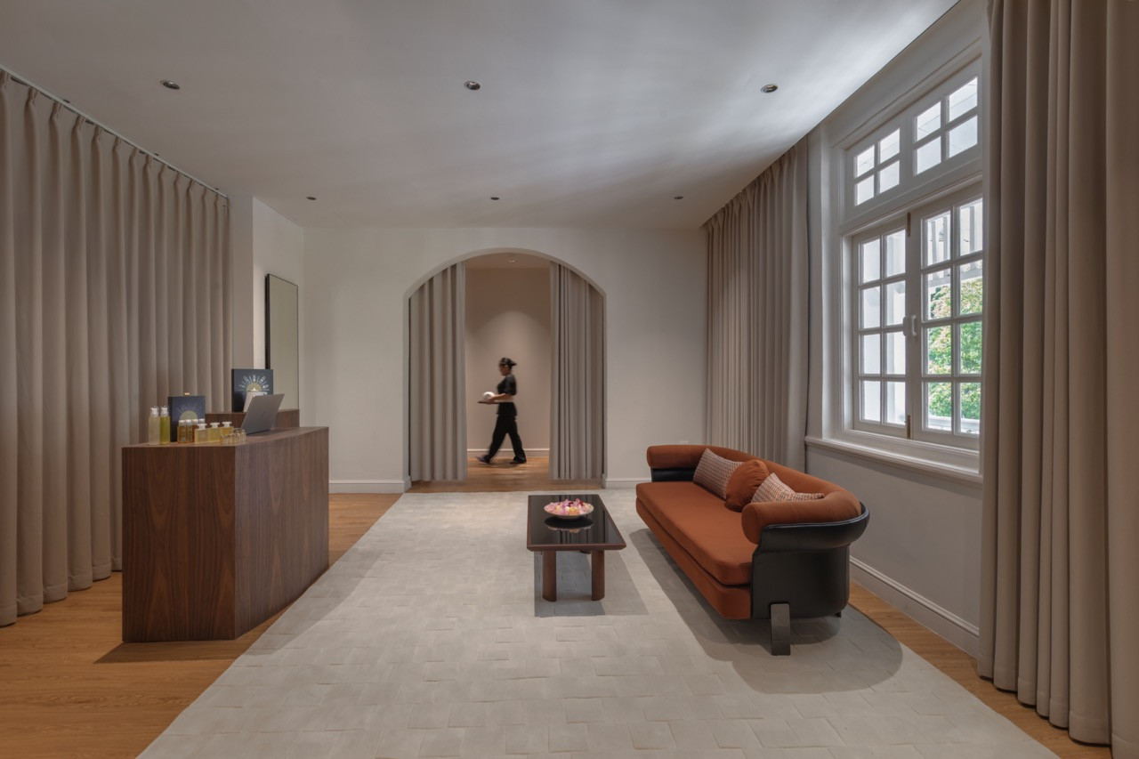The reception area of Sensorium Spa, with a walnut front desk, terracotta sofa and original casement windows; an arched passage leads to the treatment rooms beyond