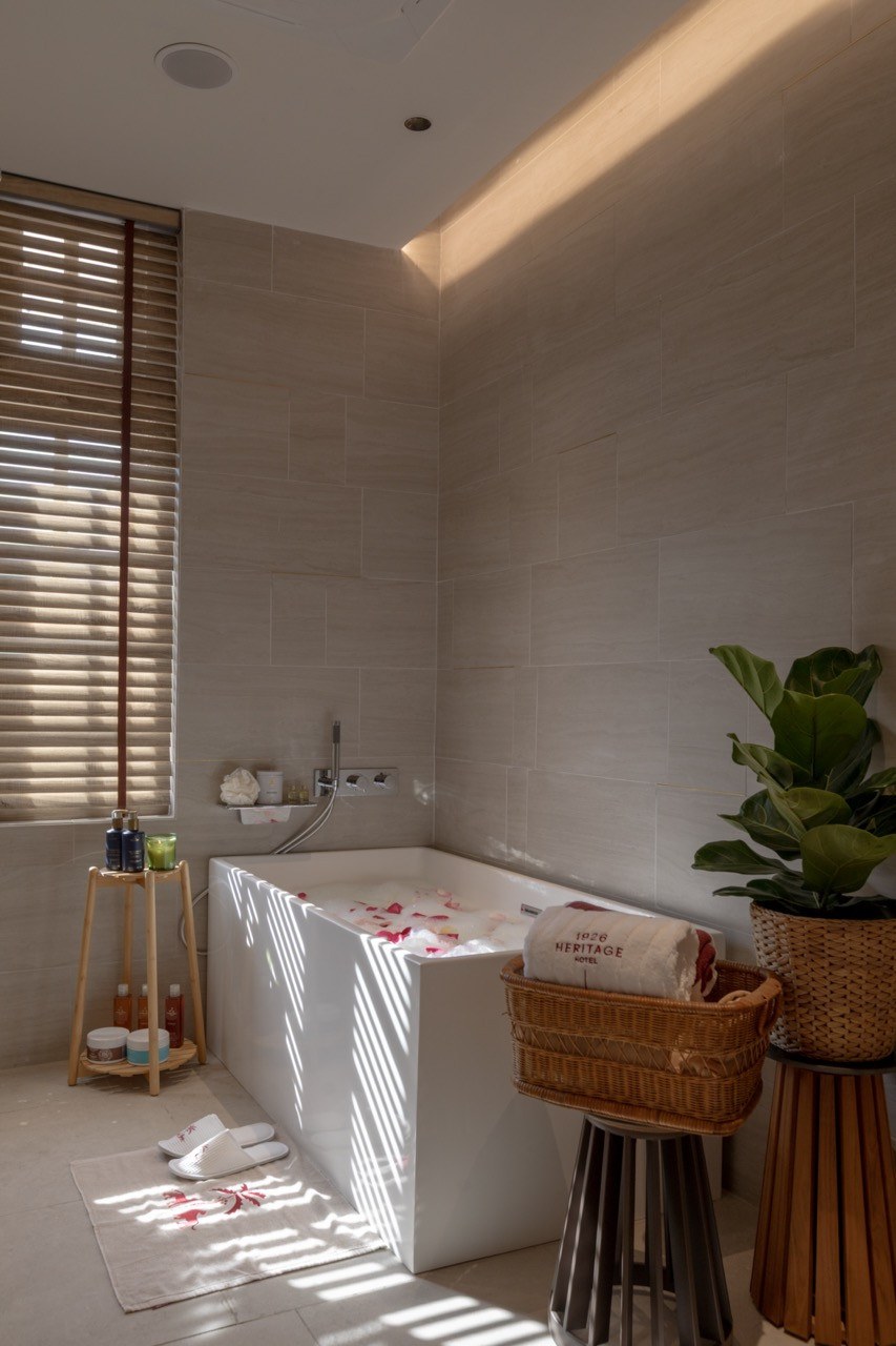 A Sensorium Spa treatment room bath, set with rose petals and louvred shutters filtering afternoon light; Sensorium products on a timber stand alongside