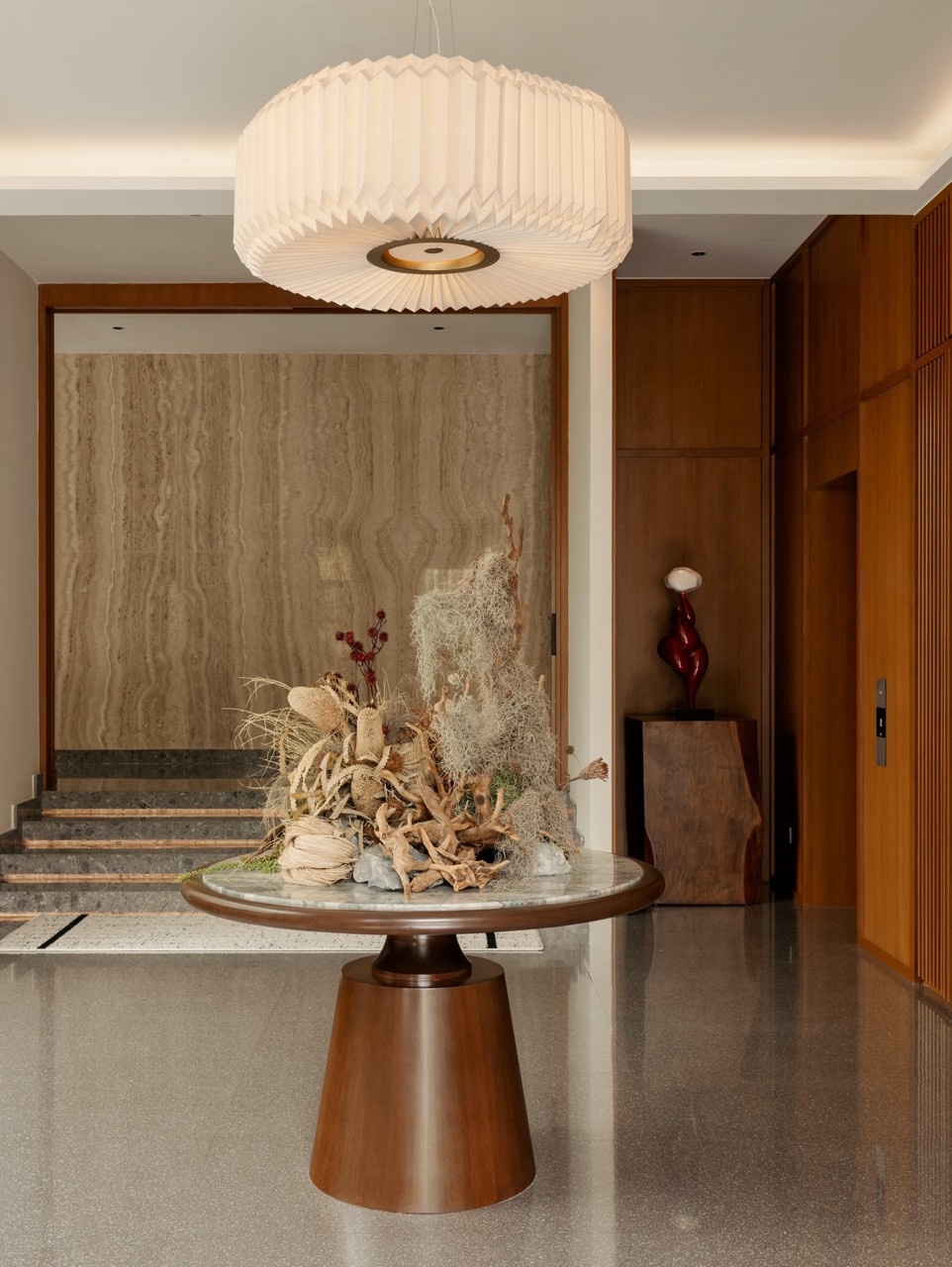 The foyer of JT House features terrazzo flooring, a travertine feature wall and solid timber joinery, with decorative styling and object curation by Lee Sin