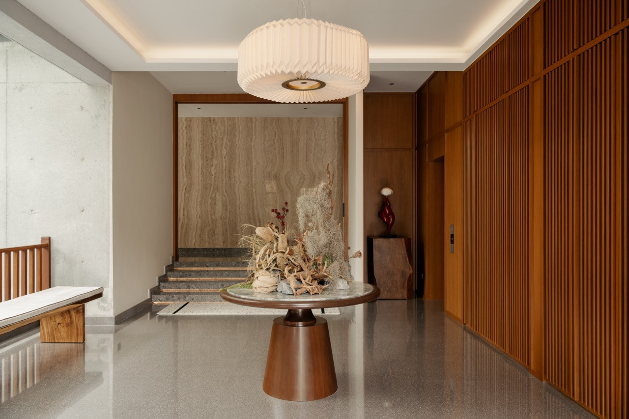 A wider view of the foyer showing the full-height timber slatted wall, terrazzo floors and travertine feature wall behind the staircase