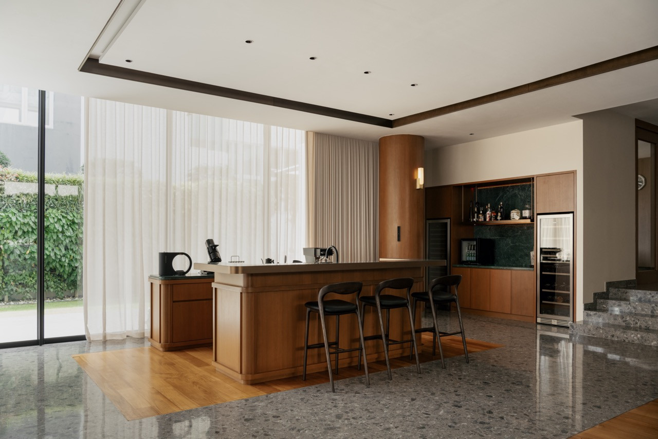 The dry kitchen features a timber island with bar seating, a green stone splashback behind the bar and sheer curtains screening the garden beyond