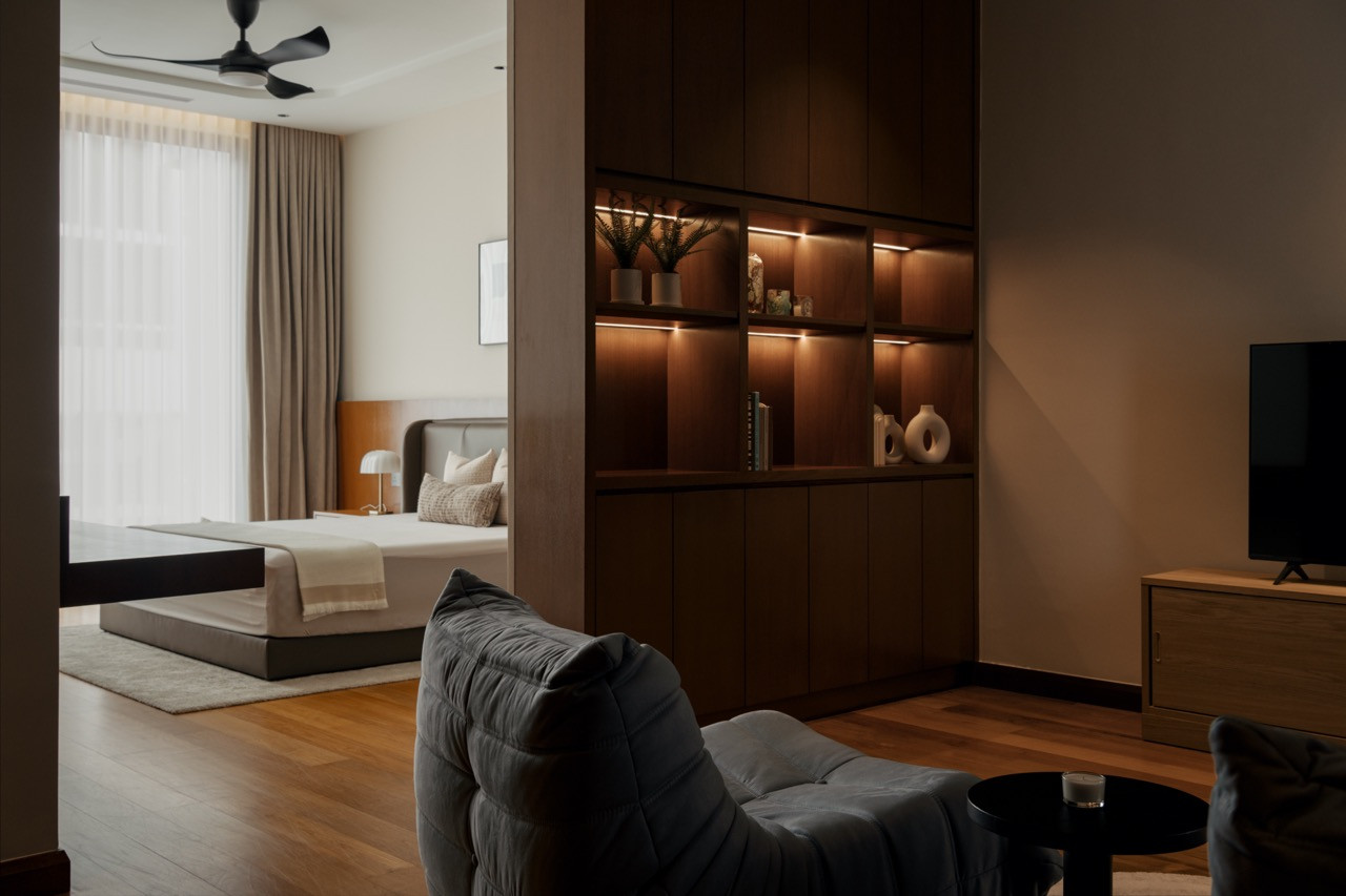 A guest bedroom on the first floor with an adjoining sitting area, separated by a backlit timber shelving unit