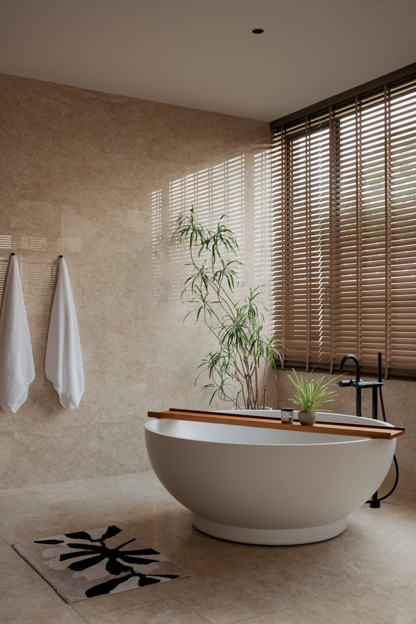 The spa-styled master bathroom on the second floor features natural stone wall and floor cladding, a freestanding bathtub and timber venetian blinds