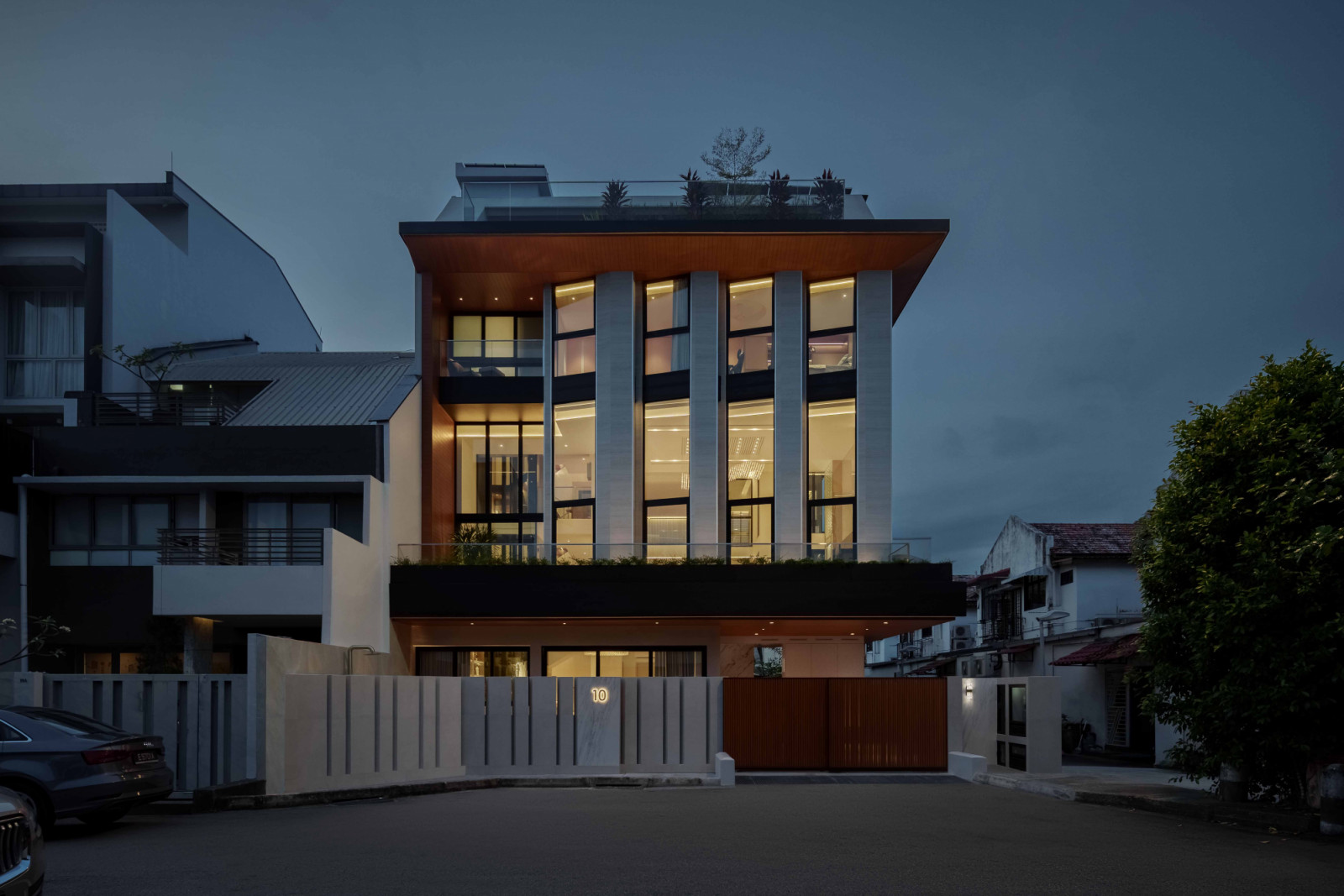 A roadside perspective of the house at dusk with windows aglow