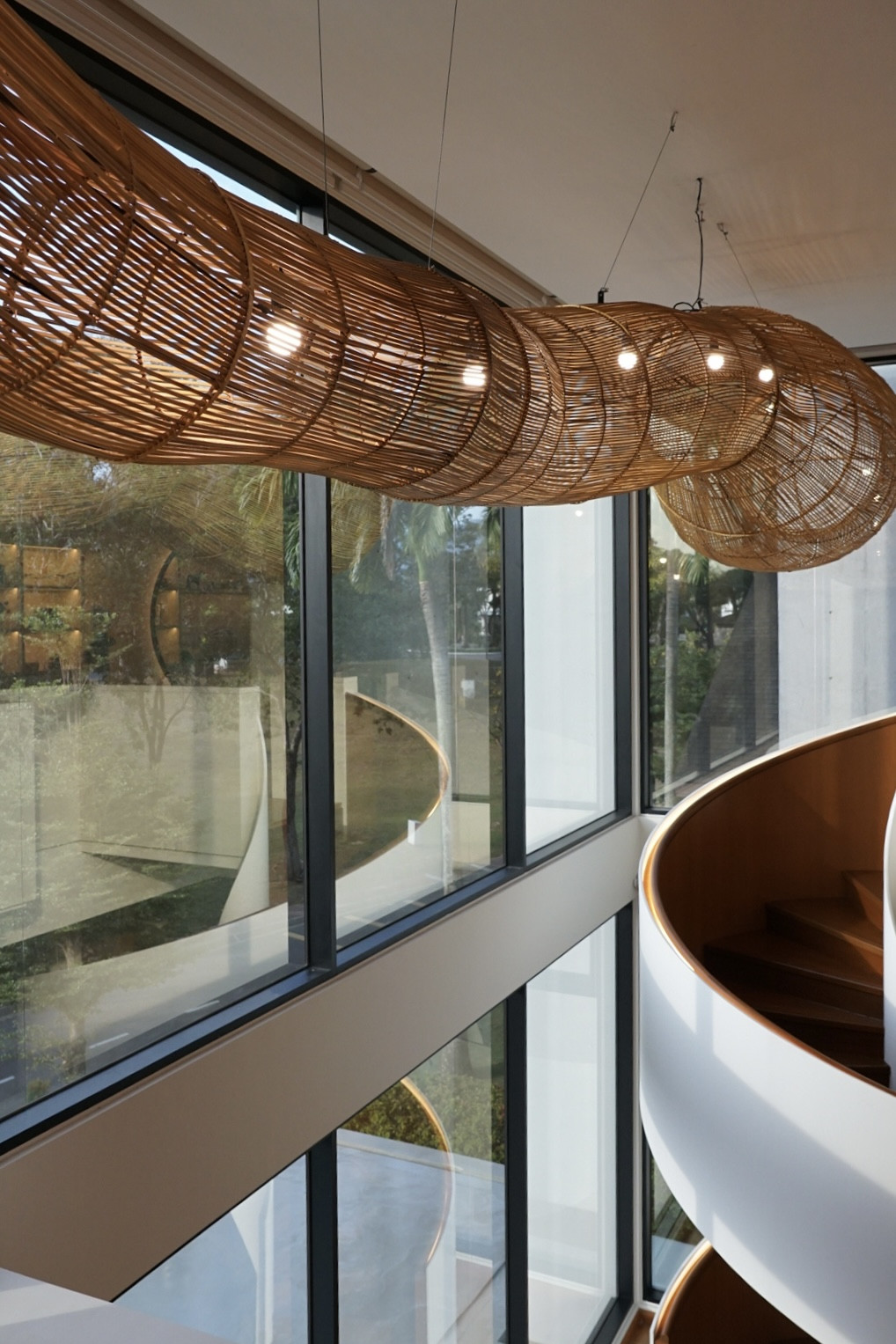 The custom thirty-foot rattan pendant installation by Rattan Art runs the length of the double-volume void alongside the sculptural spiral staircase, viewed from the first-floor landing