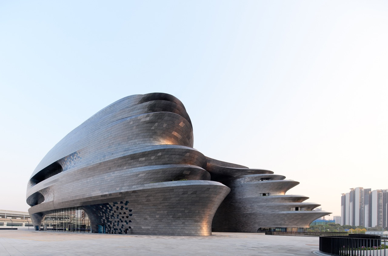 The museum’s street-level exterior at dusk, its layered steel volumes extending horizontally across the site with residential towers visible in the background (Photo: Virgile Simon Bertrand)