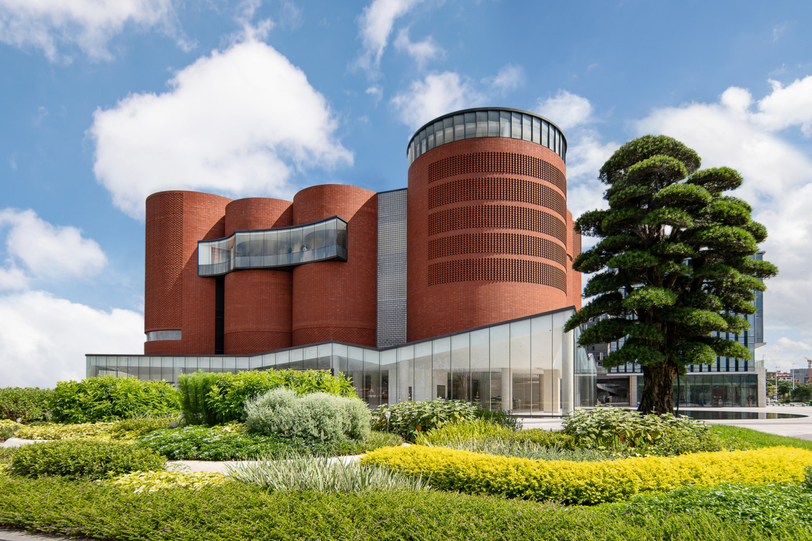 The exterior of the Xuelei Fragrance Museum in Guangzhou, its eight red-brick cylinders rising above a glazed ground-floor base and landscaped surrounds
