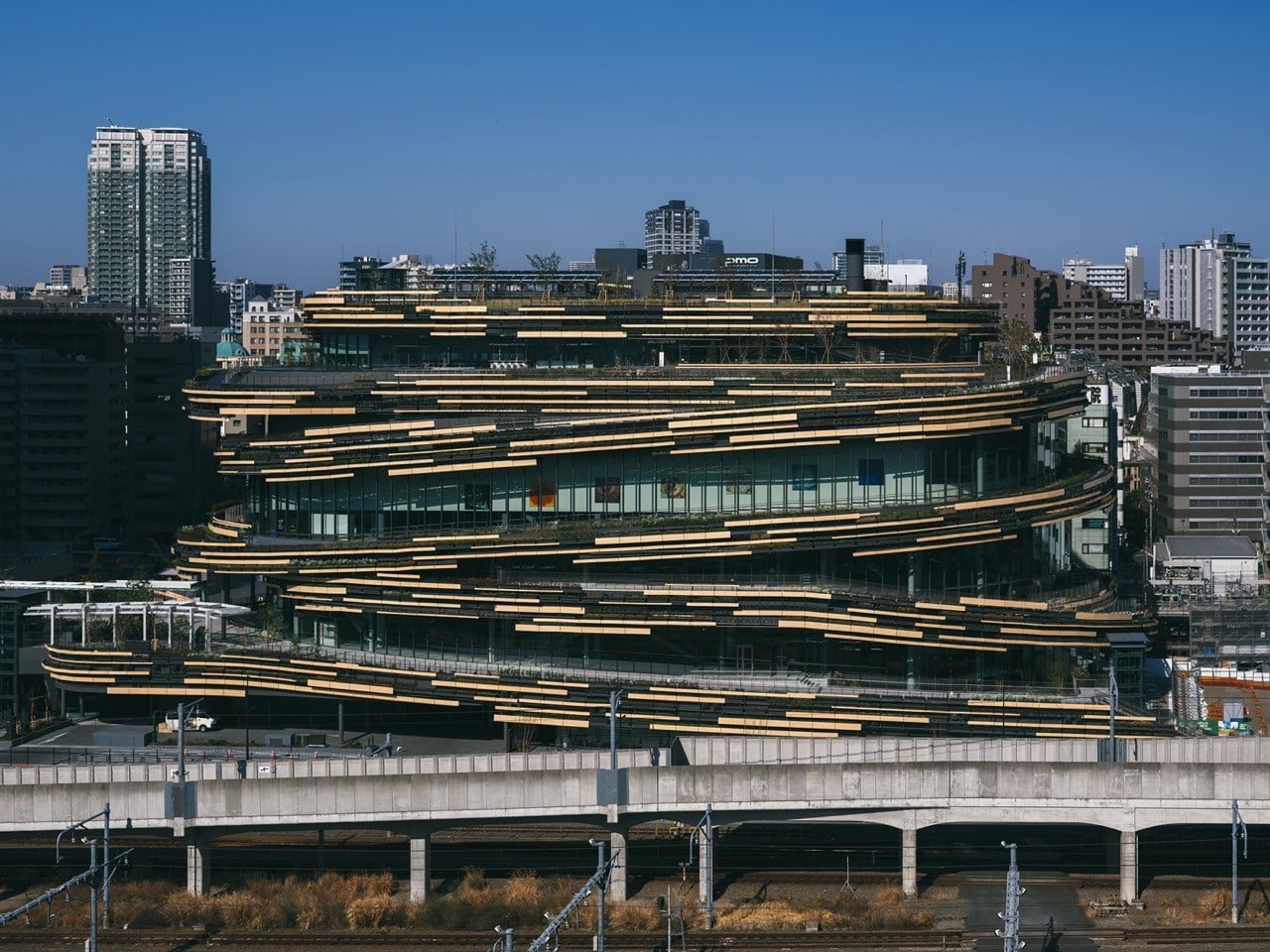 MoN Takanawa seen from across the railway lines, its spiral wood-and-glass form low against the surrounding residential and commercial blocks of Minato ward (Photo:Yasuyuki Takaki)