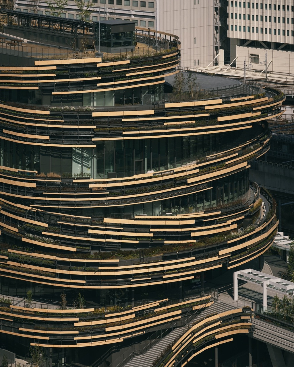 A close aerial view of MoN Takanawa’s ascending spiral facade, its horizontal wood and glass bands interspersed with planted terraces carrying more than 200 species (Photo: Yasuyuki Takaki)