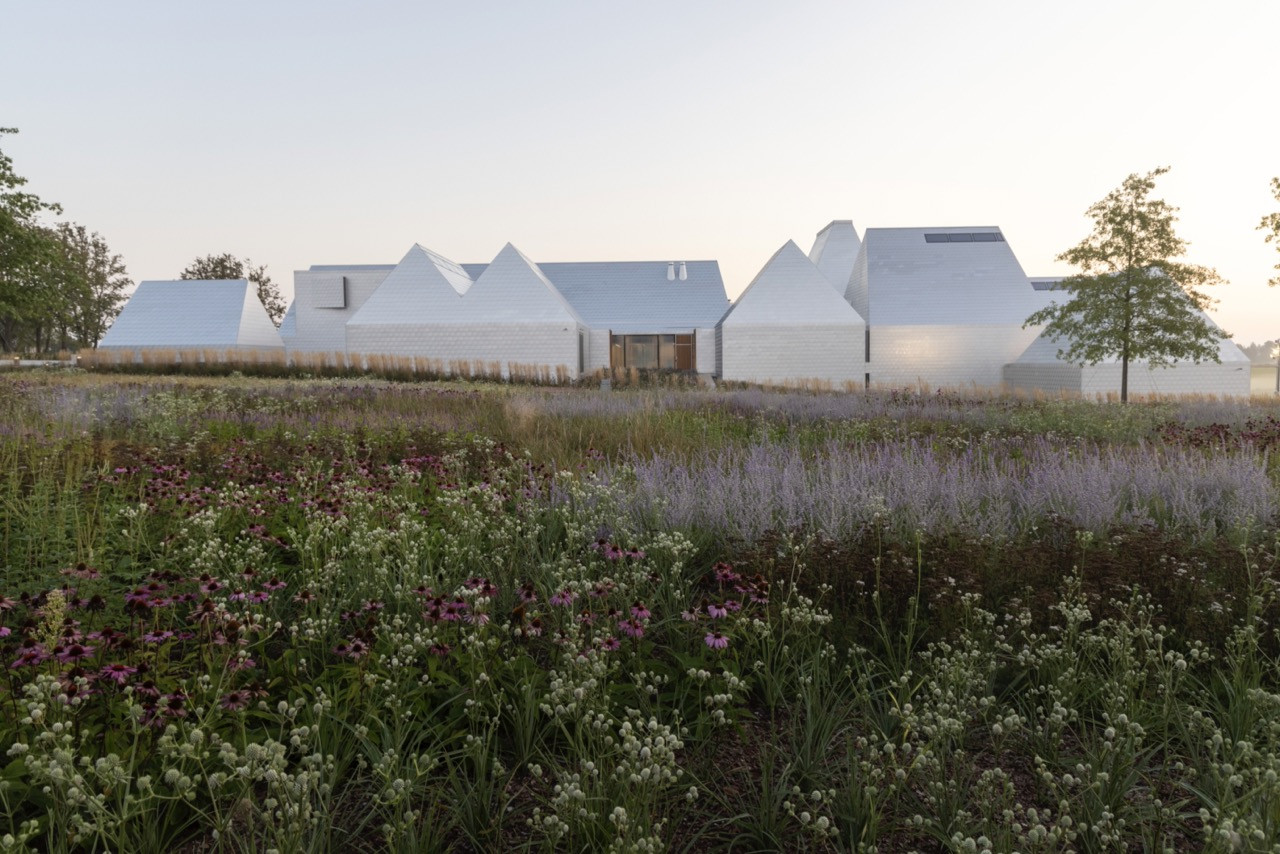 The museum’s white-tiled exterior at dusk, its irregular roofline rising and falling across the flat Lithuanian landscape amid the wildflower planting of the Memorial Park (Photo: Enea Landscape Architecture)