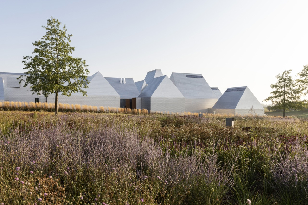 The Lost Shtetl Museum, seen across the Memorial Park meadow, its cluster of grey-tiled pitched rooflines designed by Rainer Mahlamäki to evoke the silhouette of a small village (Photo: Enea Landscape Architecture)