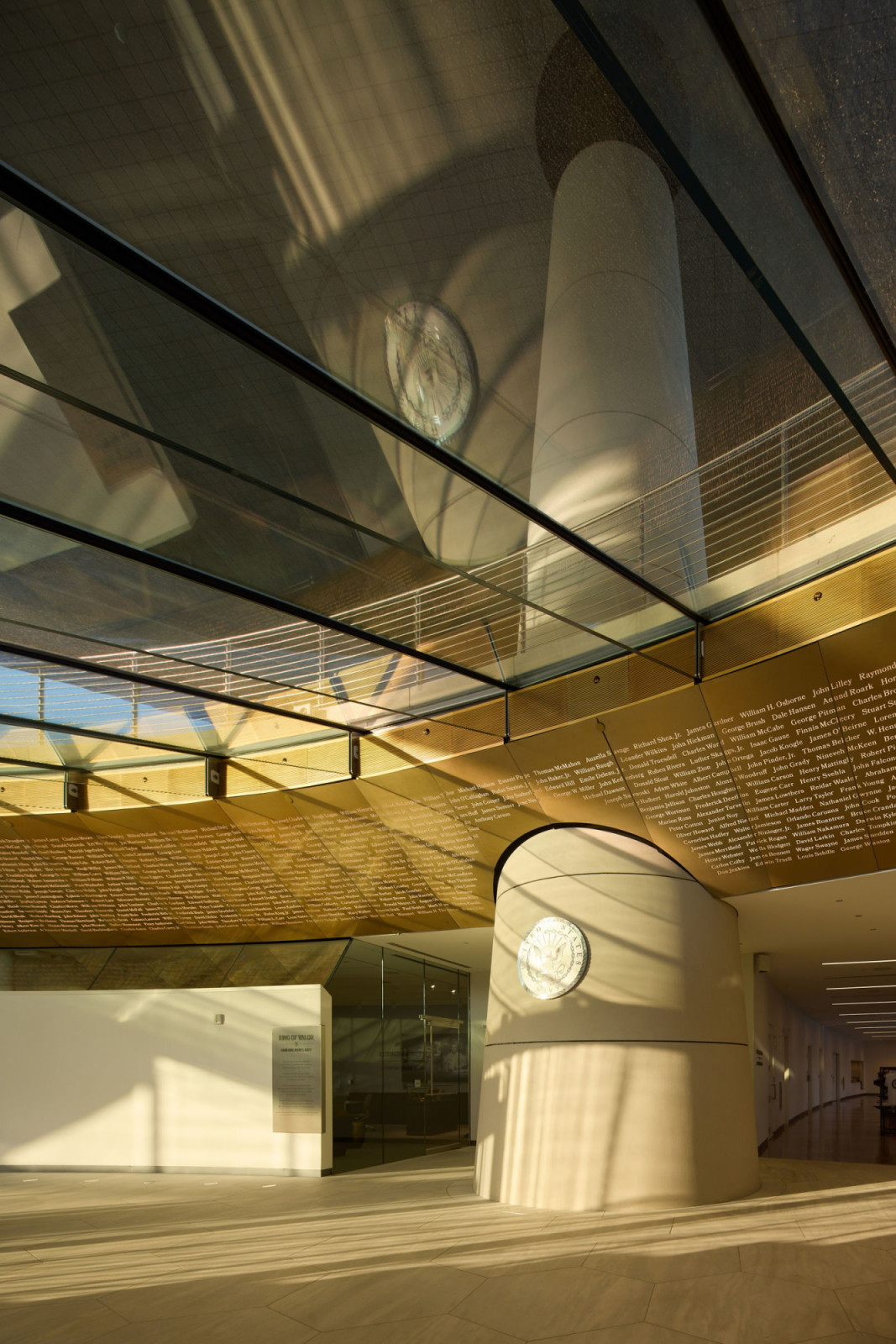 An interior view looking up through the glass floor of the Exhibition Hall, with recipient names lining the curved golden wall and the Medal of Honor seal mounted on one of the five supporting megacolumns (Photo: Corey Gaffer)