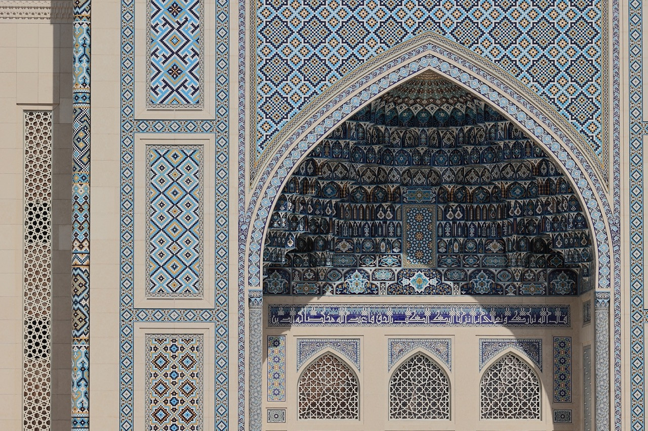 A close detail of the Center’s main portal, its pointed arch recessed within layers of hand-laid blue and white geometric tilework in the Timurid tradition