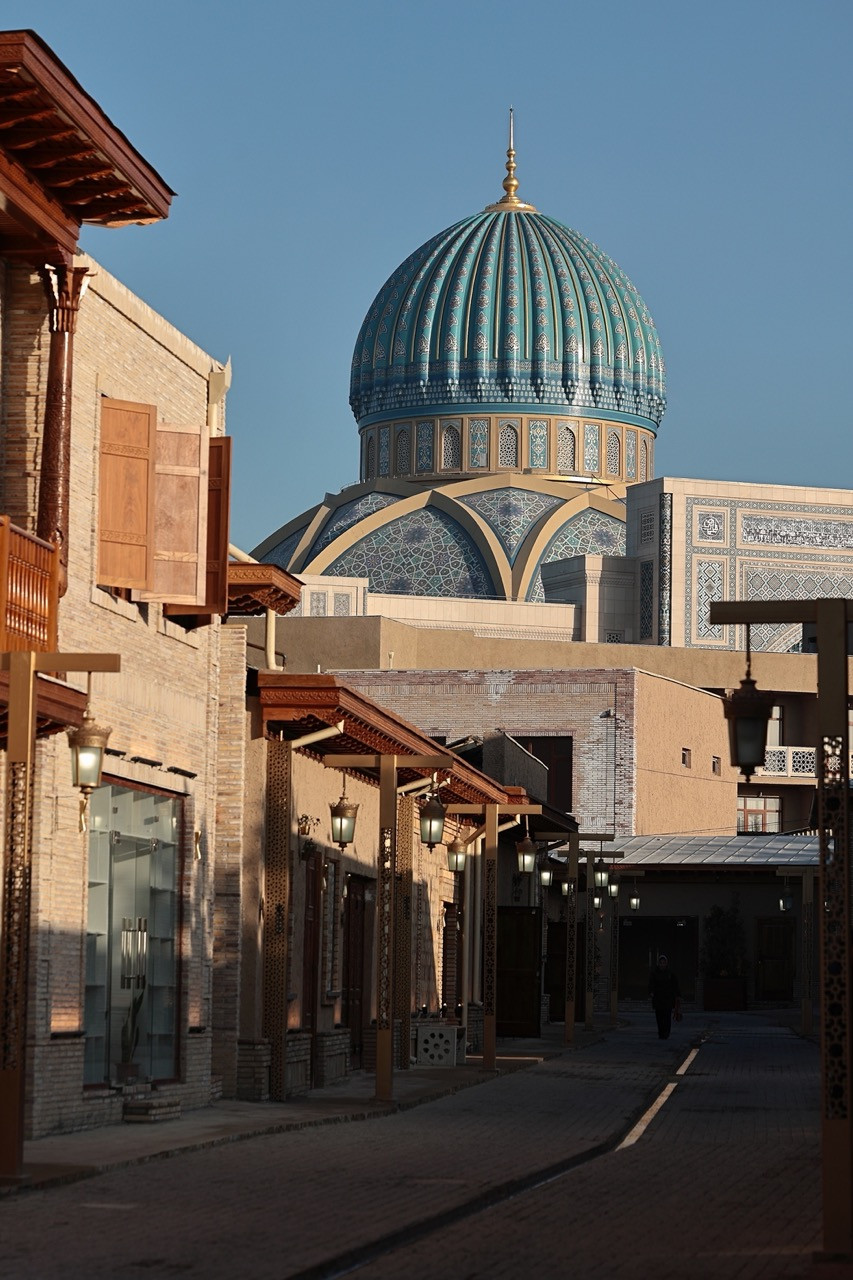 The Center’s turquoise-tiled dome is seen above a reconstructed historic street within the surrounding complex, referencing the architectural scale of Timurid-era Tashkent