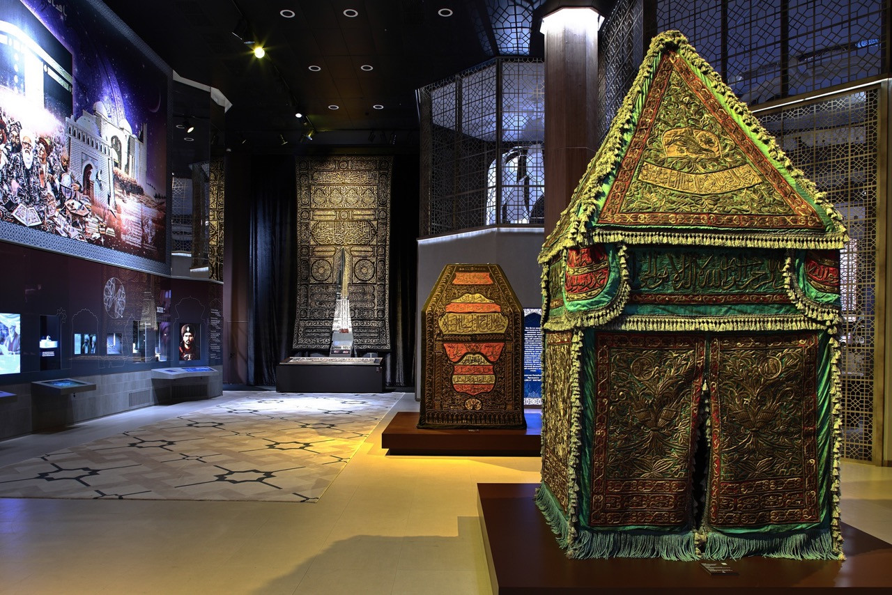 A gallery within the Center displaying embroidered textile relics and Islamic artefacts, with geometric lattice screens dividing the exhibition spaces