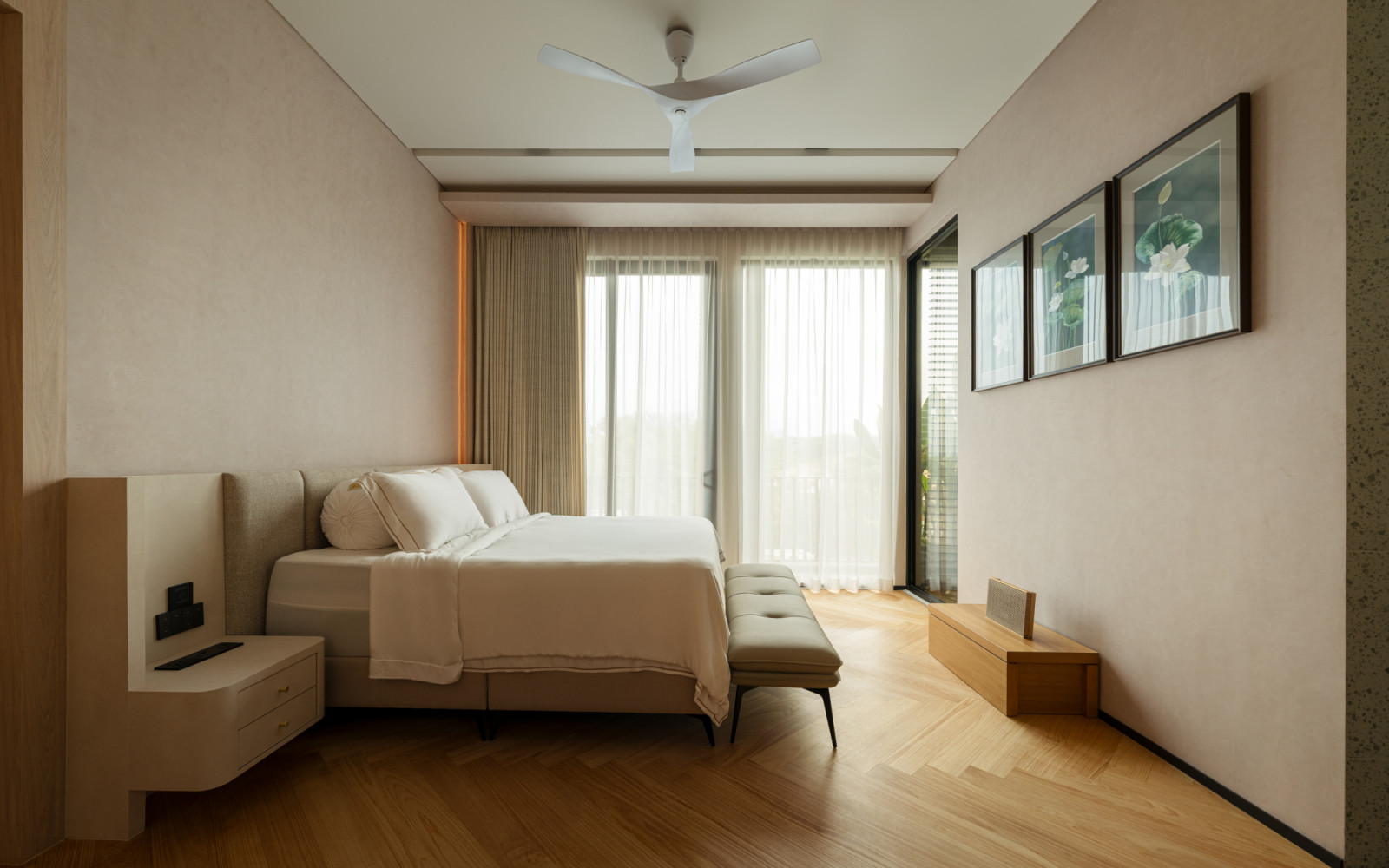 A bedroom on the upper floor with herringbone timber flooring, a linen upholstered bed, sheer curtains at the glazed balcony door and framed botanical prints on the adjacent wall