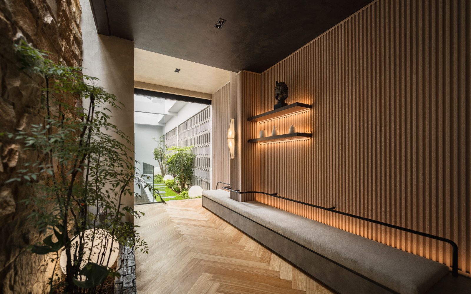 The first floor entry corridor with a timber batten feature wall and lit display shelves to the right, a planted stone niche visible through the opening to the left and herringbone timber flooring throughout