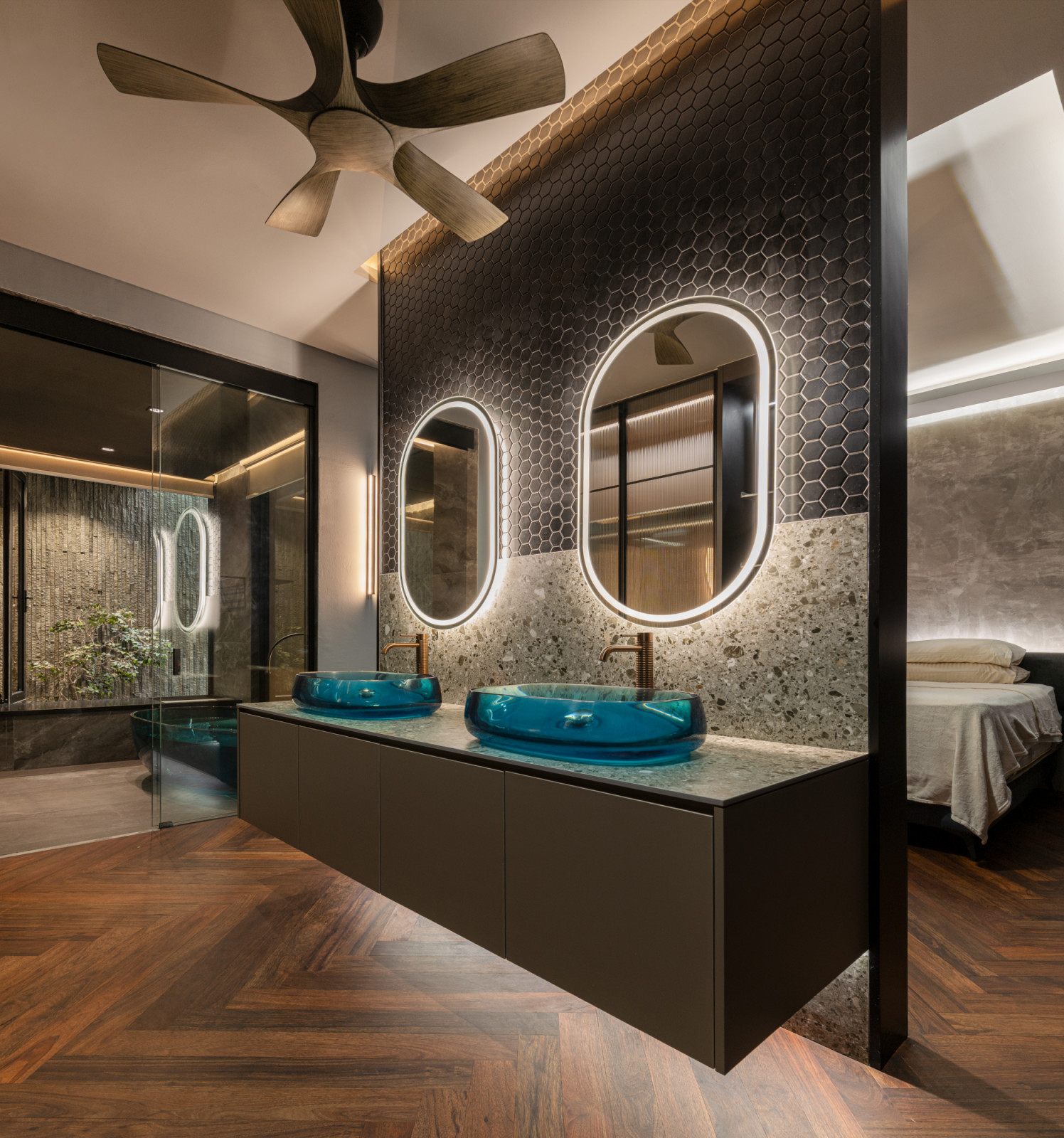 The lower ground floor bathroom features dual blue glass vessel basins on a dark floating vanity, a hexagonal mosaic feature wall with oval backlit mirrors, and a view through to the lava stone air well beyond