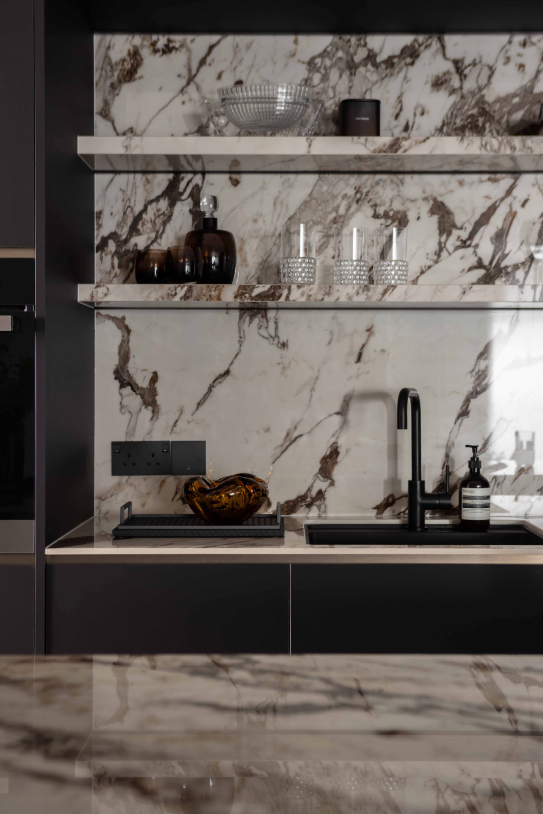 Set against darker cabinetry and black fittings, the marble-look surface adds both brightness and drama