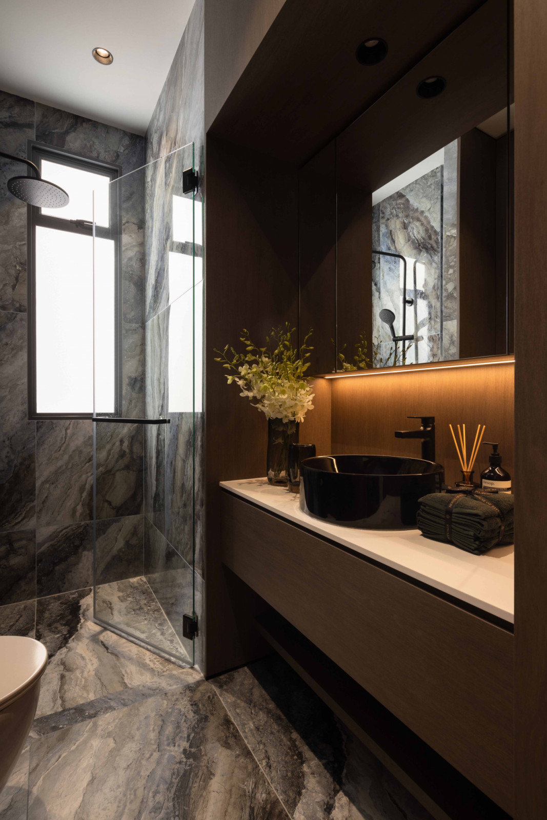 Stone-look surfaces, fluted glass, bronze-toned accents, dark cabinetry and warm integrated lighting were specifically used to create a hotel-like ambience