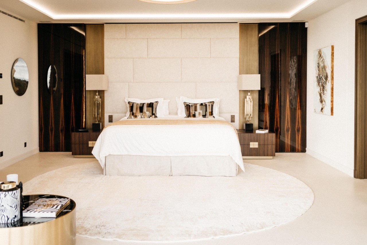 The principal bedroom with a full-height upholstered headboard wall flanked by polished Macassar ebony wardrobe panels