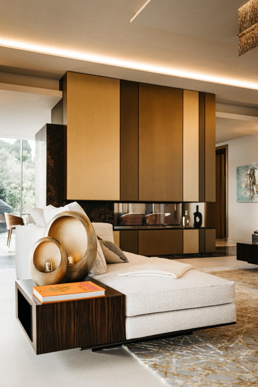 The living room with a cream chaise longue, brass sculptural lamp and double-sided fireplace with brushed brass cladding