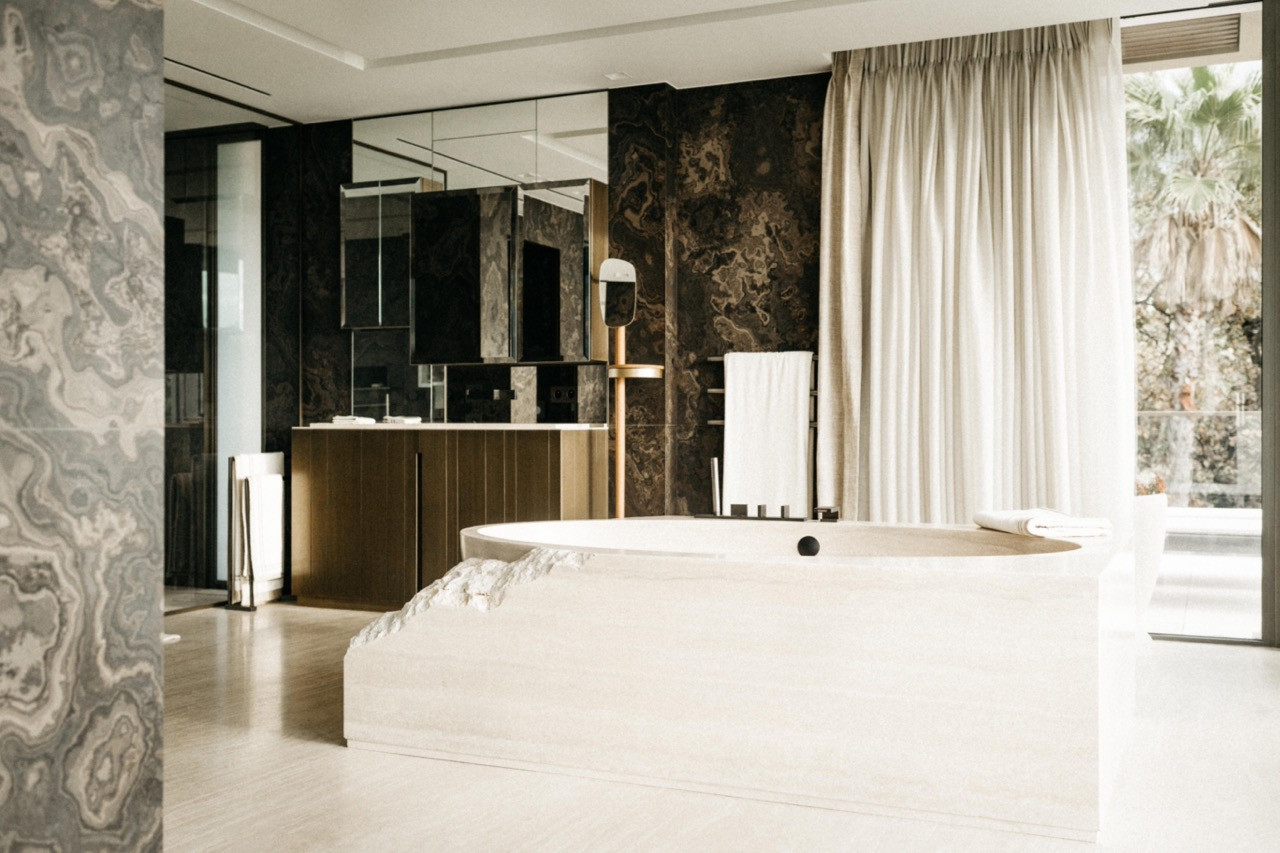 The principal bathroom with freestanding travertine bathtub, oak vanity unit and dark figured marble wall cladding
