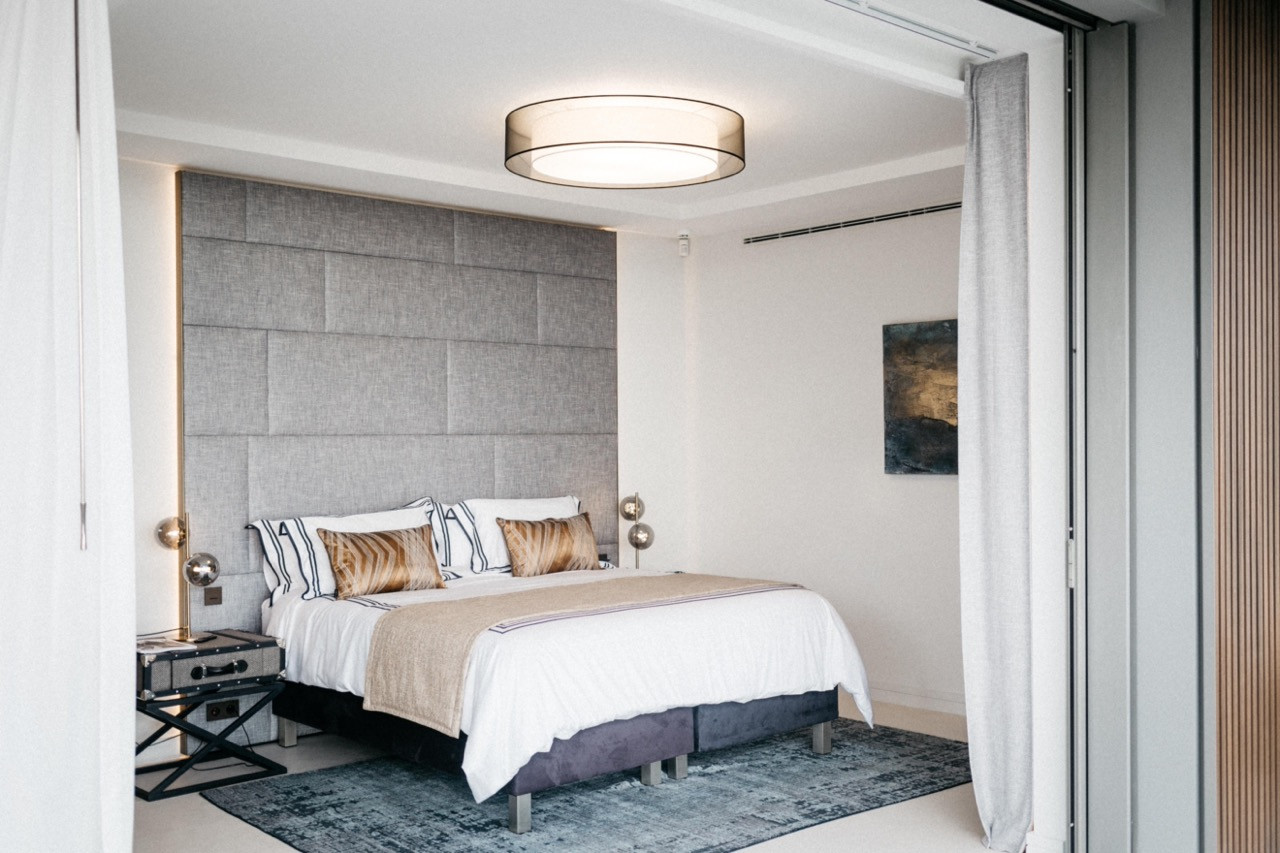 A guest bedroom with a tall grey upholstered headboard panel and vintage-style bedside tables