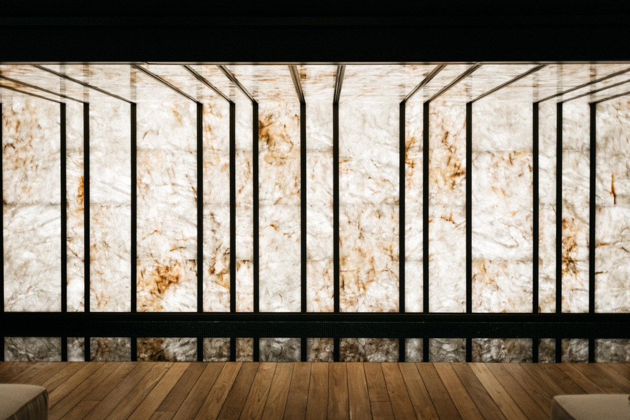 The full span of the backlit stone wall, divided by a black metal framework, anchors the basement spa